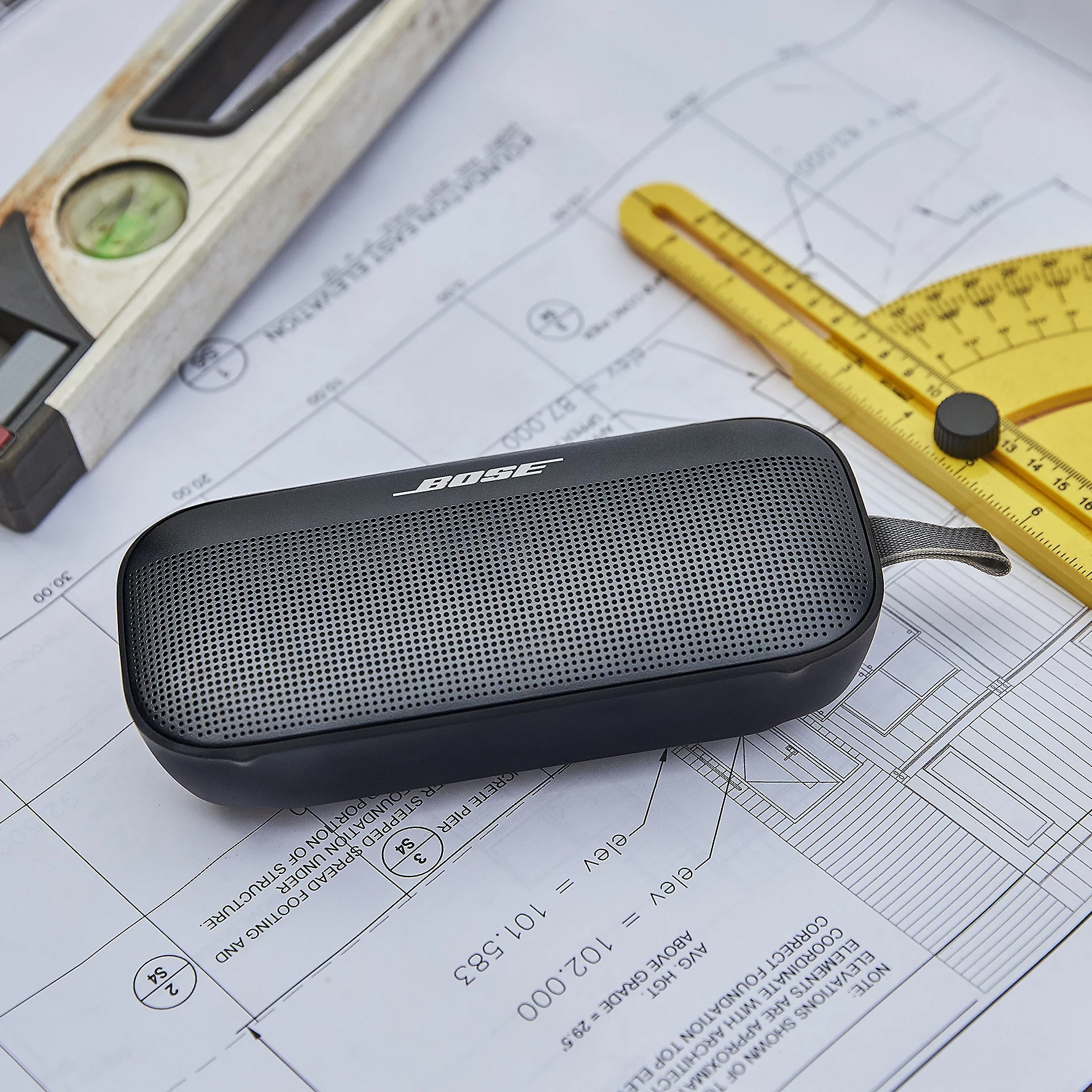 A Bose portable speaker on top of architectural drawings with a level tool and protractor.