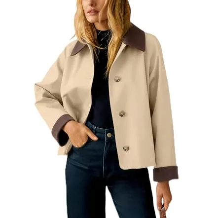 A woman wears a beige button-up jacket with a dark collar and cuffs, paired with dark jeans and a black top.