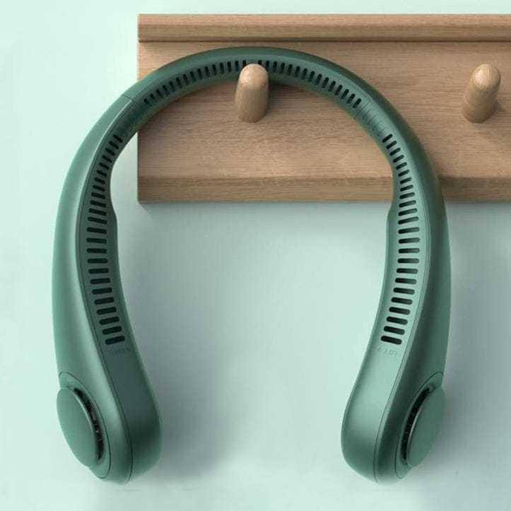 A green, neck-mounted personal fan with vents along its inner curve and circular ends, hung on a wooden peg rack.