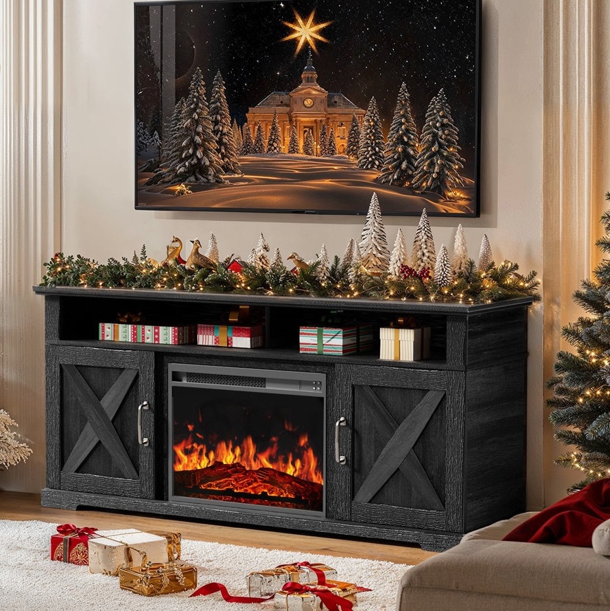 Black TV stand with an electric fireplace, decorated with Christmas garland, miniature trees, and bird figurines. A holiday-themed image of a snowy scene is displayed on the TV above. Wrapped gift boxes are arranged around the area.