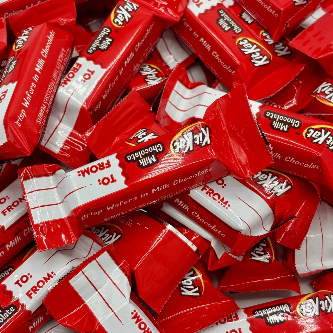 Red and white Kit Kat candy wrappers featuring \“TO: FROM:\“ labels, intended for gifting purposes, display the words \“Crisp Wafers in Milk Chocolate.\“