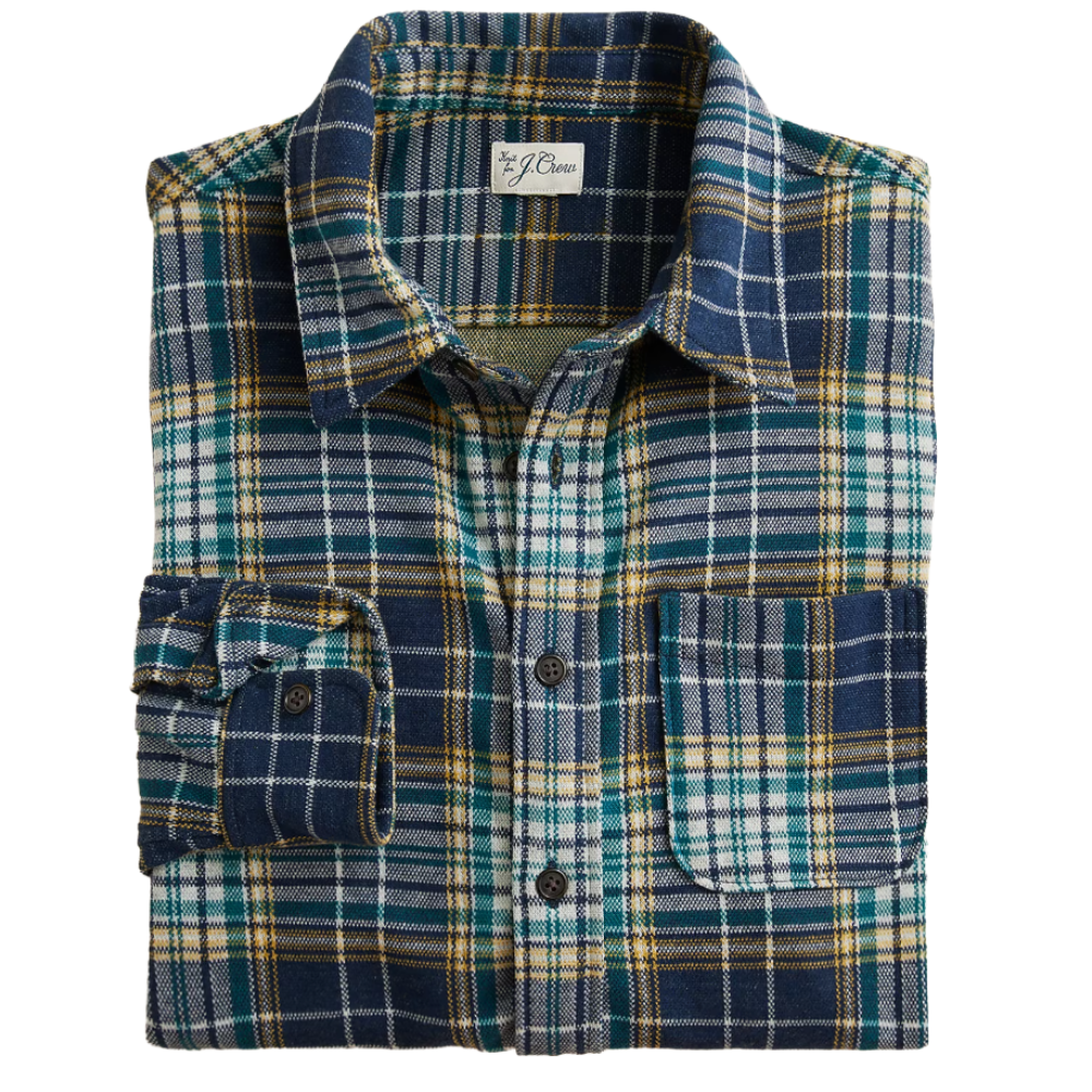 A folded plaid flannel shirt featuring blue, green, and yellow checkered patterns with a front pocket and button closure.