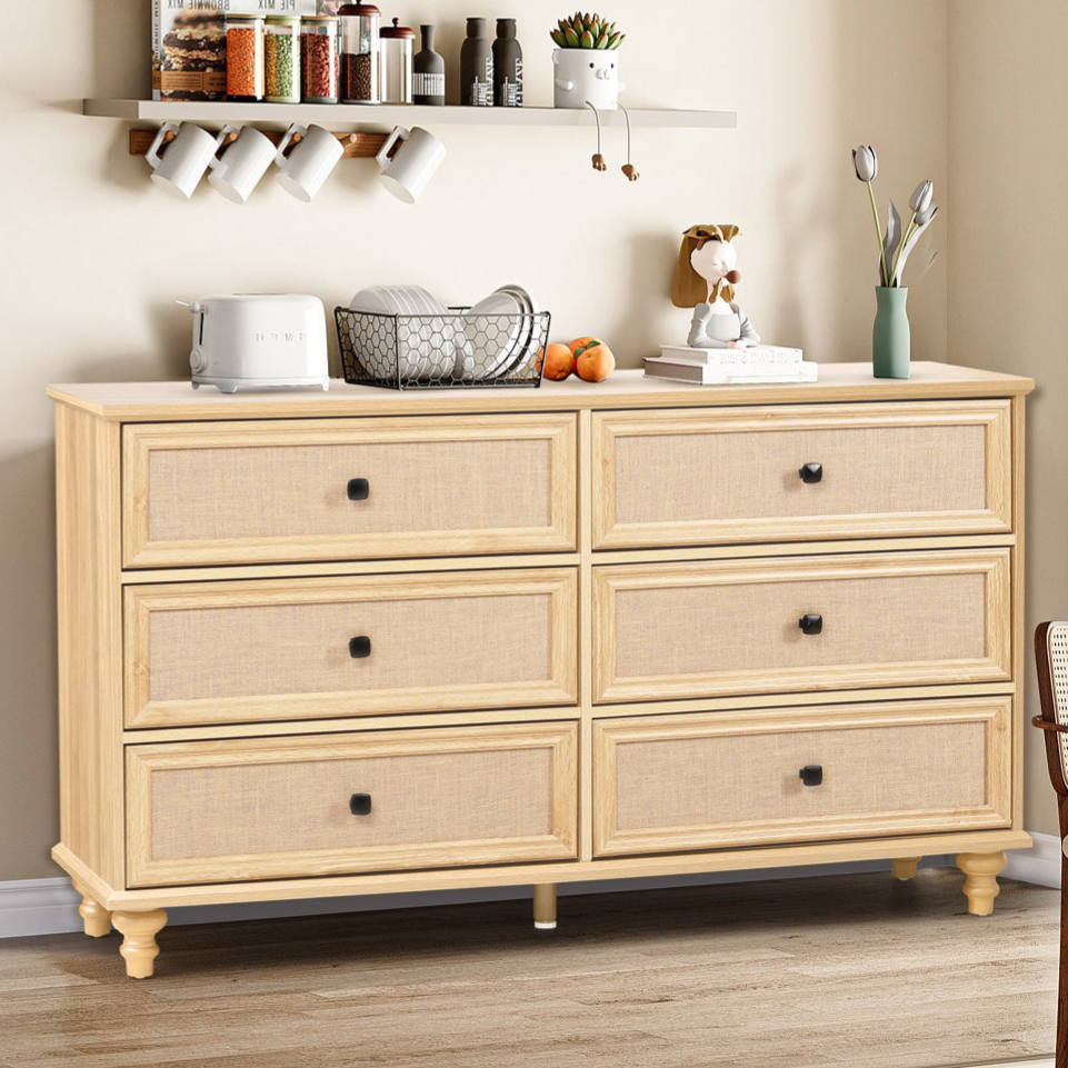 A wooden dresser with six drawers topped with a toaster, a wire basket with dishes, and a small vase. Above, two shelves hold jars, mugs, and small decorations. A chair with a woven seat sits nearby, under a window with blinds.