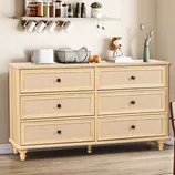 A wooden dresser with six drawers topped with a toaster, a wire basket with dishes, and a small vase. Above, two shelves hold jars, mugs, and small decorations. A chair with a woven seat sits nearby, under a window with blinds.