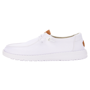 White slip-on shoes with a canvas upper, featuring a moccasin-style stitching, lace accents, and a cushioned sole. Small brown leather patches add detail on the tongue and heel.