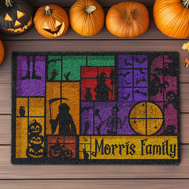 A Halloween-themed doormat featuring colorful blocks with silhouettes of spooky figures such as a skeleton, witch, bats, and pumpkins. Decorated with carved pumpkins on a wooden surface.