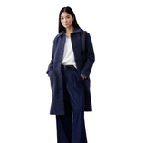 A woman wears a dark blue overcoat, white top, wide-legged denim pants, black belt, and black shoes, carrying a black bag on her shoulder.