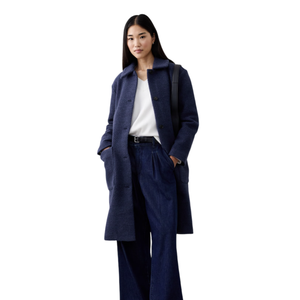 A woman wears a dark blue overcoat, white top, wide-legged denim pants, black belt, and black shoes, carrying a black bag on her shoulder.