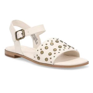 White sandal with brass-colored studs on a wide front strap, adjustable ankle strap with buckle, and flat wooden sole.