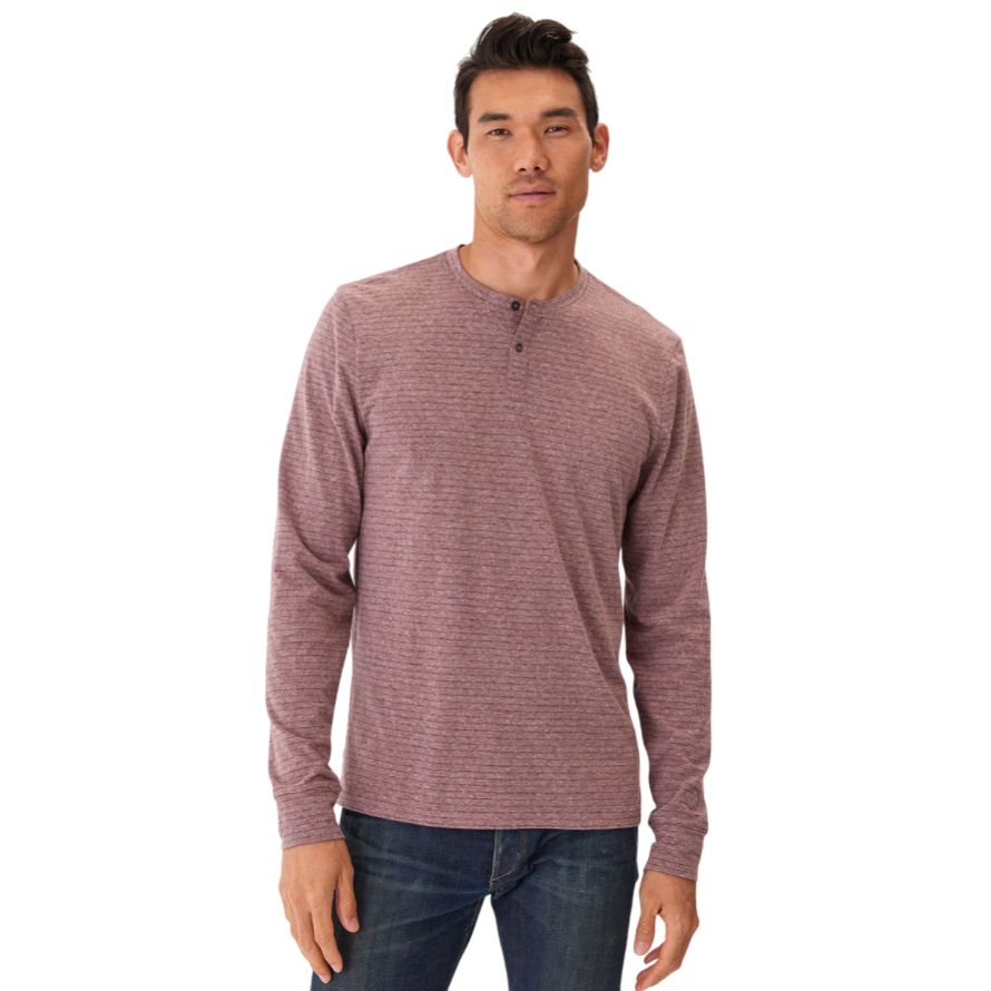 A man is wearing a long-sleeve, heathered henley shirt in a muted purple color paired with dark blue jeans.