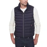 A man wearing a navy quilted vest over a cream cable-knit sweater and dark jeans.