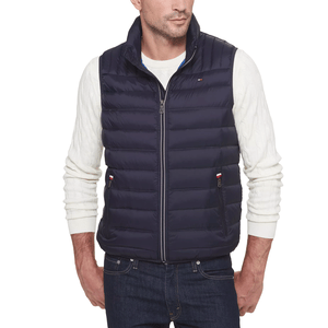 A man wearing a navy quilted vest over a cream cable-knit sweater and dark jeans.