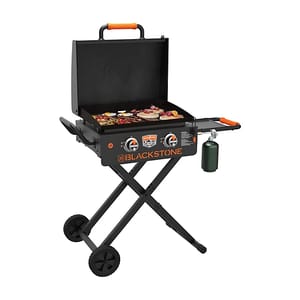 A Blackstone portable griddle with two burners, collapsible legs, and a propane tank, set up for grilling various foods.