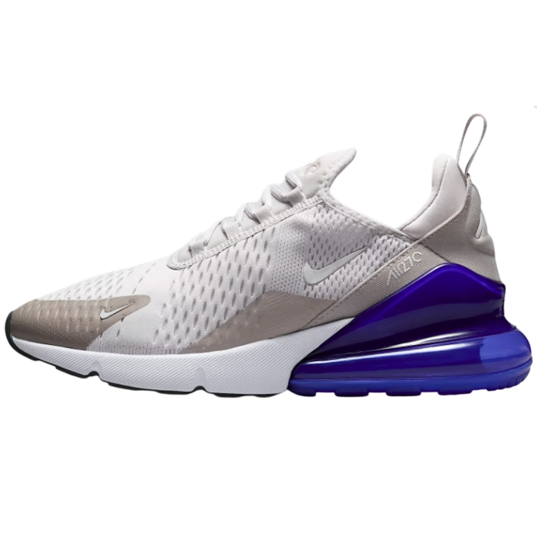 The Nike Air Max 270 features a mesh upper in white and beige tones, with a prominent purple Air unit in the heel for cushioning. The shoe includes white laces, a pull tab on the heel, and a sleek athletic design.