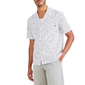 Short-sleeve, white camp collar shirt with a gray floral pattern, featuring front buttons and a relaxed fit. Worn over a white tee, paired with light gray pants.