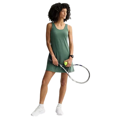A woman stands holding a tennis racket and ball, wearing a green sleeveless dress and white sneakers.
