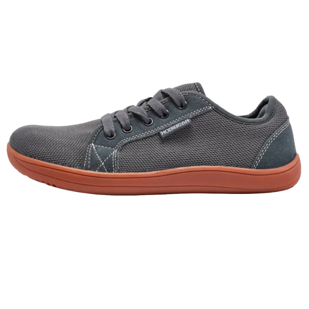 Gray casual sneaker with a dark orange rubber sole and black laces; features a textured fabric upper and a small tab on the side.