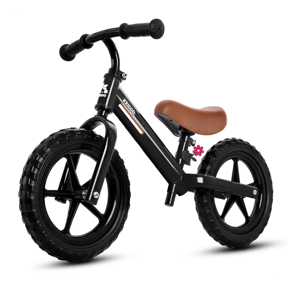 A black balance bike with a brown saddle, black handlebars, and thick black tires, featuring a small decorative flower detail.