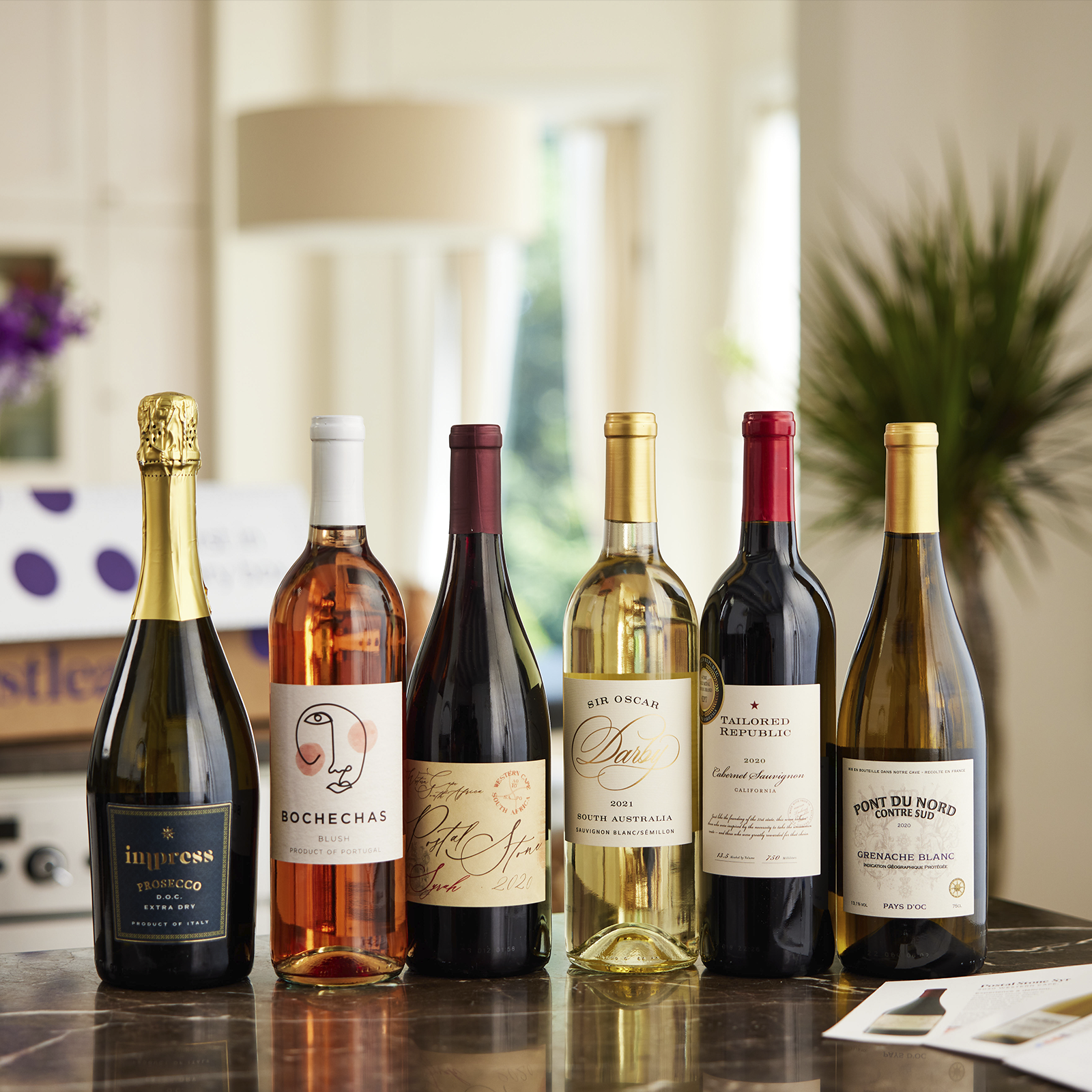 A selection of six wine bottles: Impress Prosecco, Bochechas Blush, Petit Etoile Pinot Noir, Sir Oscar Sauvignon Blanc Semillon, Tailored Republic Cabernet Sauvignon, and Pont Du Nord Grenache Blanc.