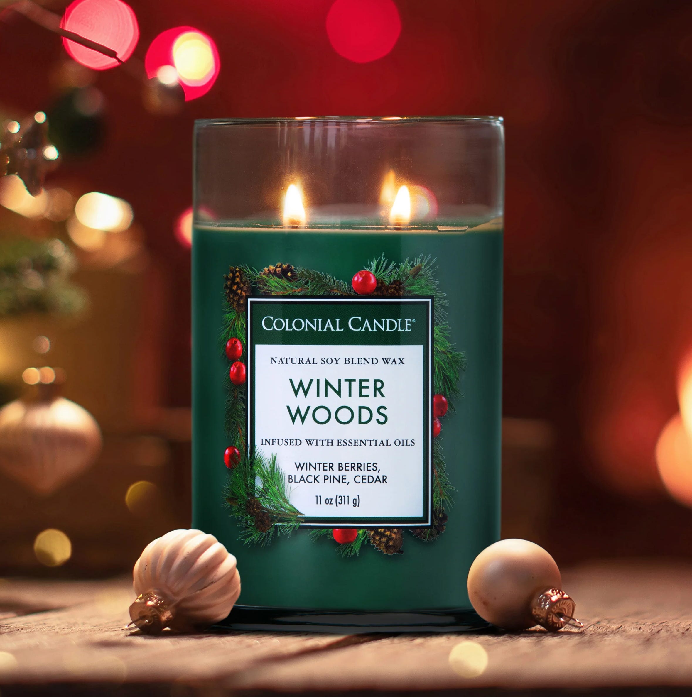 A green \“Winter Woods\“ candle by Colonial Candle, featuring natural soy blend wax infused with essential oils. Fragrance notes include winter berries, black pine, and cedar; size: 11 oz (311 g).