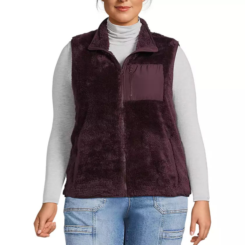 A woman is wearing a burgundy fleece vest with a zipper and chest pocket, paired with a light gray turtleneck and blue jeans.