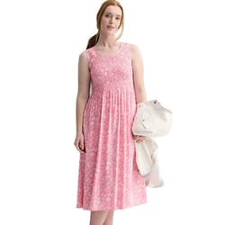 A woman wearing a sleeveless pink floral dress holds a white jacket draped over one arm.