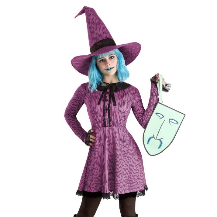 A person in a purple witch costume with a pointed hat and blue wig holding a comical sad face mask.