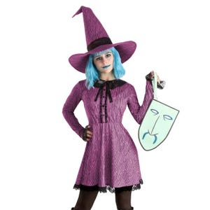 A person in a purple witch costume with a pointed hat and blue wig holding a comical sad face mask.