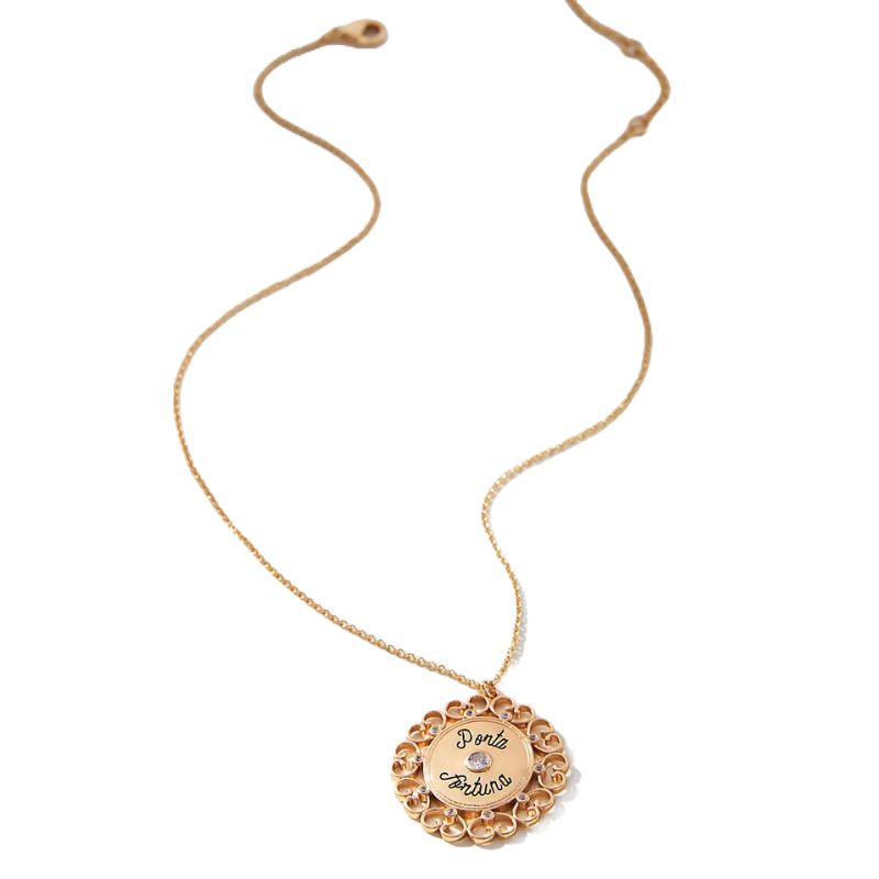 A gold necklace features a decorative round pendant with intricate designs and the inscription \“Porta Fortuna\“ along with a small gemstone in the center.