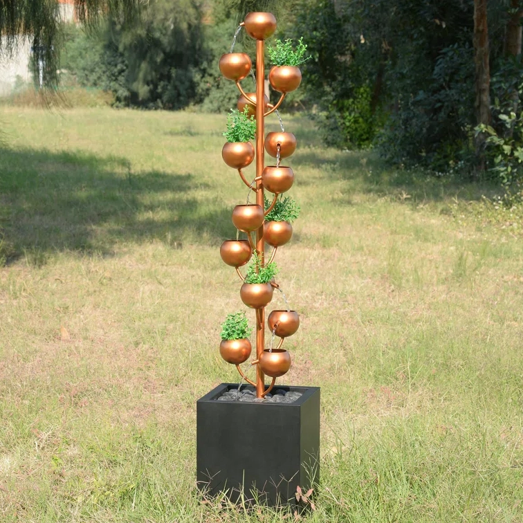 A decorative copper rain chain with bowls and green accents, standing in a square black base.
