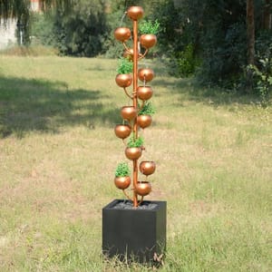 A decorative copper rain chain with bowls and green accents, standing in a square black base.
