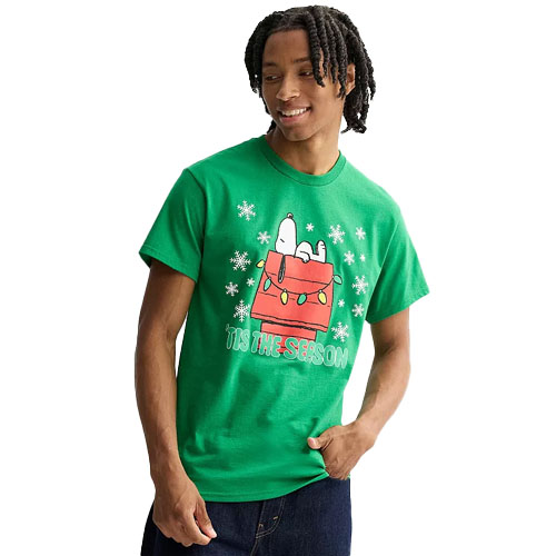 A man wears a green T-shirt featuring Snoopy on a red doghouse, surrounded by snowflakes, with the text \“Tis The Season.\“