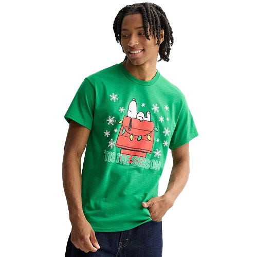 A man wears a green T-shirt featuring Snoopy on a red doghouse, surrounded by snowflakes, with the text \“Tis The Season.\“