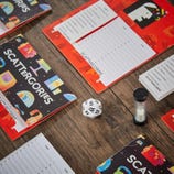 Classic Scattergories game includes pads with category lists, a 20-sided letter die, a sand timer, and game folders. Players roll the die to select a letter, then write words starting with that letter for each category before time runs out.