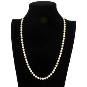 A single strand of white pearls is displayed elegantly on a black bust stand, showcasing a classic and timeless jewelry piece.