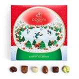 Godiva limited edition advent calendar features a festive snowy village with penguins. Includes a selection of assorted chocolates displayed below the calendar.