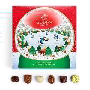 Godiva limited edition advent calendar features a festive snowy village with penguins. Includes a selection of assorted chocolates displayed below the calendar.