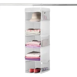 A hanging fabric organizer with five open shelves holds various items like a hat, folded clothes, and shoes. Two mesh side pockets store smaller accessories.
