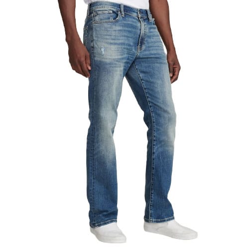 A person wearing light-wash straight-leg jeans paired with white slip-on shoes.