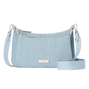 The Kate Spade Duet Denim Crossbody is a light blue handbag with a textured front, featuring silver-tone hardware and a detachable strap. It has two zipper compartments and a branded plate on the front.