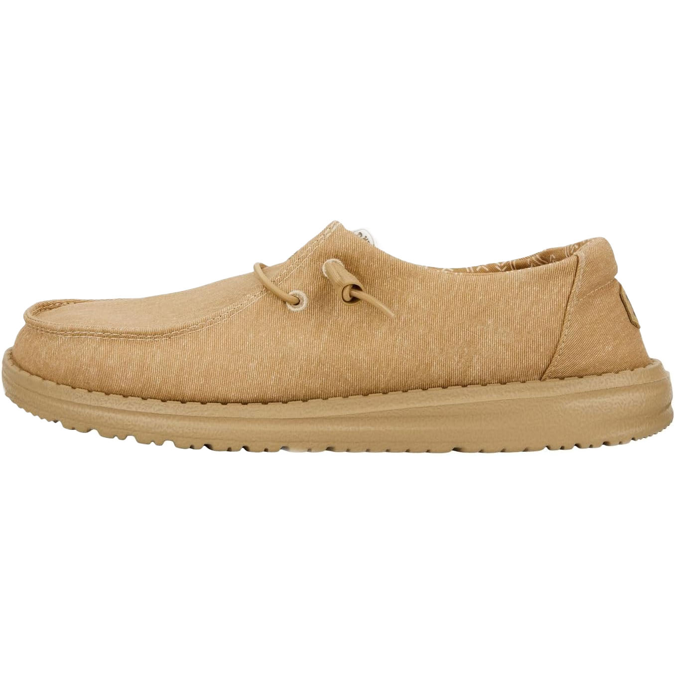 Hey Dude Wendy Chambray Loafers feature a lightweight, casual slip-on design in a tan color with canvas material and a cushioned sole for comfort. They include lace detailing and a textured rubber outsole for grip.