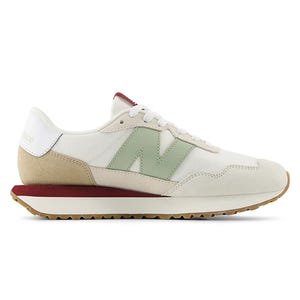 A sneaker featuring a soft beige and white color scheme with a green \“N\“ logo, beige suede accents, a maroon heel strap, and a textured tan outsole.