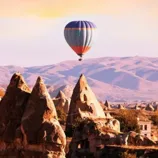 A hot air balloon floats over Cappadocia's unique rock formations during sunset, showcasing the region's scenic beauty and iconic landscapes.