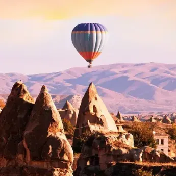 A hot air balloon floats over Cappadocia's unique rock formations during sunset, showcasing the region's scenic beauty and iconic landscapes.