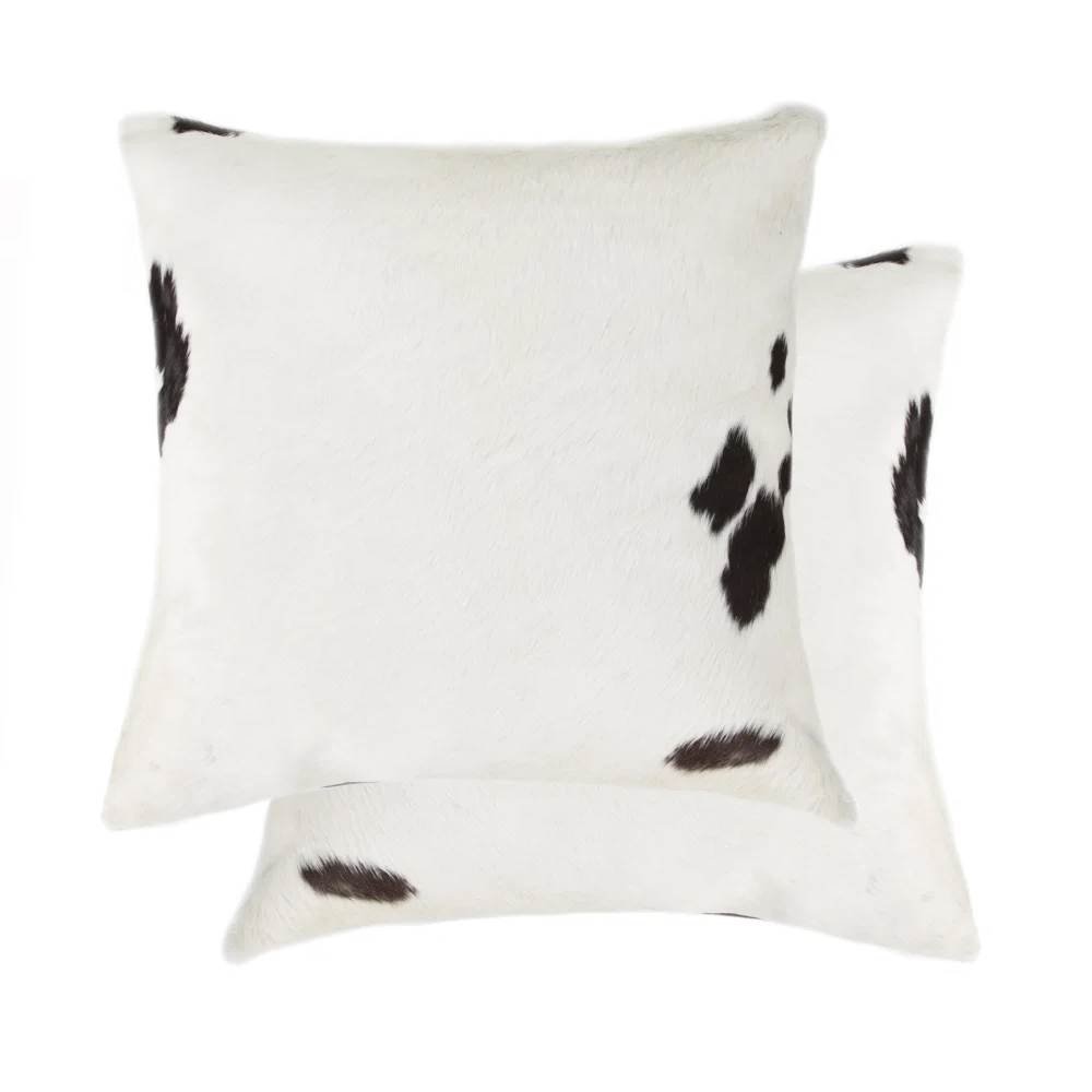 Two square cowhide-patterned pillows with a white base and dark brown spots.