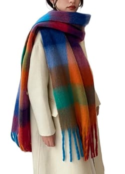 A person wears a thick, multicolored plaid scarf with a long fringe, paired with a light cream coat.