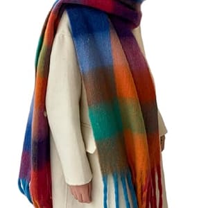 A person wears a thick, multicolored plaid scarf with a long fringe, paired with a light cream coat.