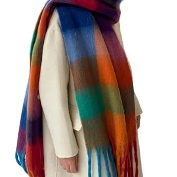A person wears a thick, multicolored plaid scarf with a long fringe, paired with a light cream coat.