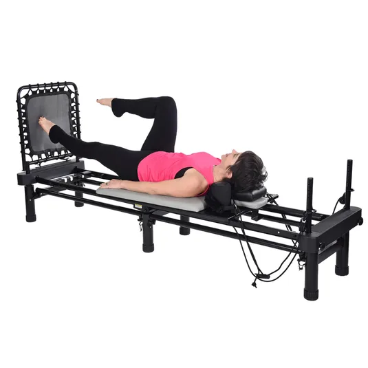 A person is exercising on a Pilates reformer machine with a rebounder attachment, wearing a pink top and black leggings, lying on their back with legs in motion.
