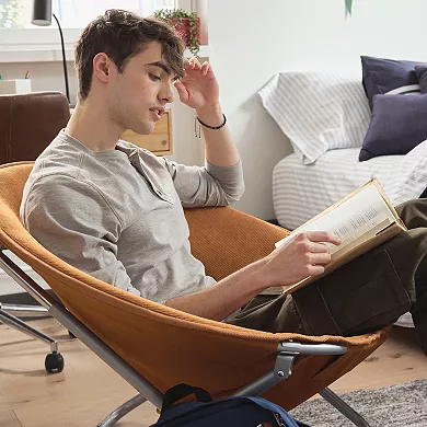 A man is seated in a foldable saucer chair made with a metal frame and cloth cover, suitable for casual indoor seating.